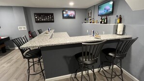 A modern kitchen with a granite countertop, black bar stools, and a TV mounted above the counter.
