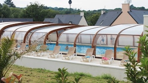 Zona junto a la piscina con sillones de descanso y una piscina techada.