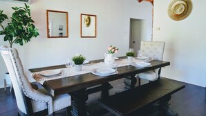 Un comedor con una mesa de madera dispuesta para cuatro personas, dos sillas, una planta en maceta y un espejo en la pared.