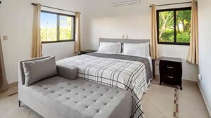 A bedroom with a bed, a sofa, a nightstand, and two windows with curtains.