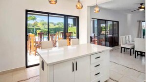A spacious kitchen with a large island, sliding glass doors leading to an outdoor area with a pool, and a dining area with white furniture.
