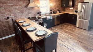 A modern kitchen with a brick wall, stainless steel appliances, and a wooden dining table set for four. - Spacious ‘GEM’ of the city (Geneva)
