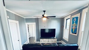 A compact living space with a dark wood floor, a black sofa, a flat-screen TV, and a ceiling fan. - Spacious ‘GEM’ of the city (Geneva)
