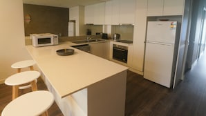 A modern kitchen with a central island, wooden stools, a microwave, a sink, a stove, and a refrigerator. - Modern 3-bedroom townhouse in central Cape Woolamai (Cape Woolamai)