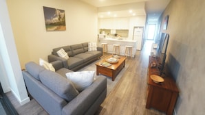A modern living room with a grey sofa set, a wooden coffee table, and a kitchen area in the background. - Modern 3-bedroom townhouse in central Cape Woolamai (Cape Woolamai)