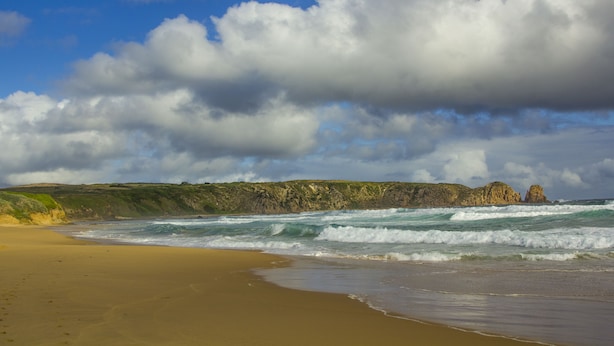 A beach with waves, a sandy shore, and a rocky cliff in the background. - Modern 3-bedroom townhouse in central Cape Woolamai (Cape Woolamai)
