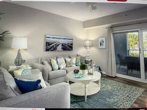 A living room with a sofa, a coffee table, and a painting on the wall. - Updated rates:Oceanwalk bldg 2: 2 bed 2 bath w Ocean view from balcony. Pet fee (New Smyrna Beach)