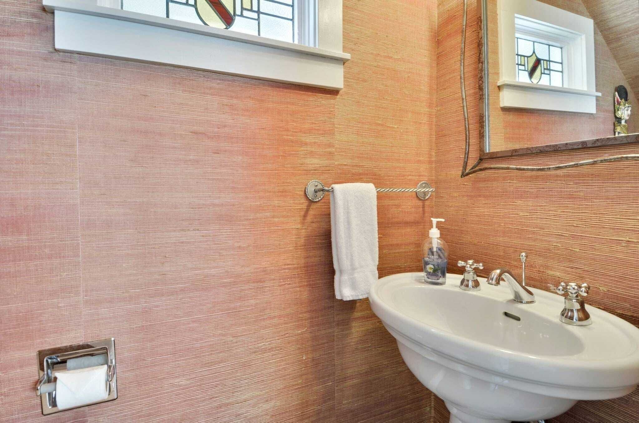 Un bagno con un lavandino bianco, un portasciugamani, un dispenser di sapone e una finestra con decorazioni in vetro colorato.