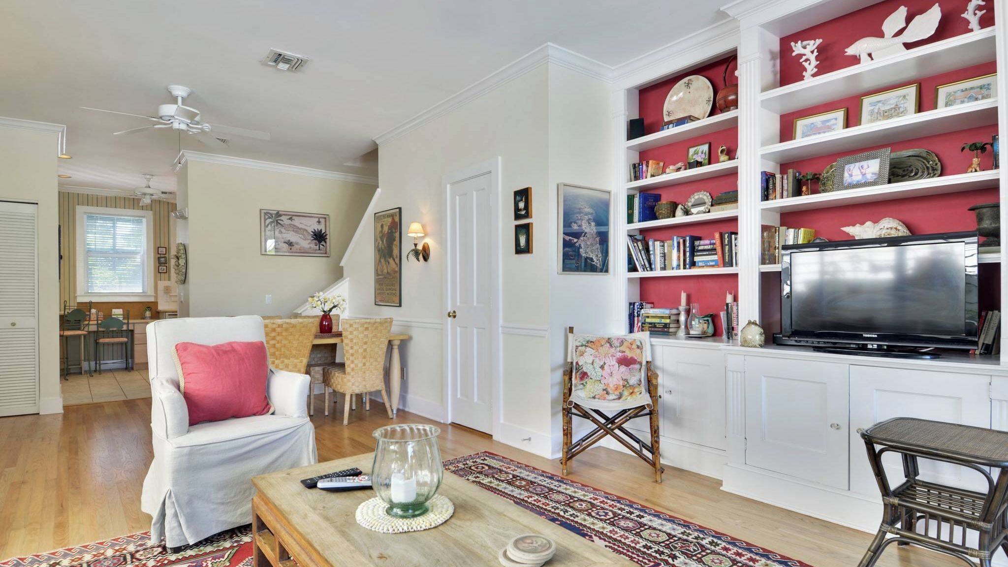 A living room with a white sofa, a television, a bookshelf, and a dining area with a table and chairs.