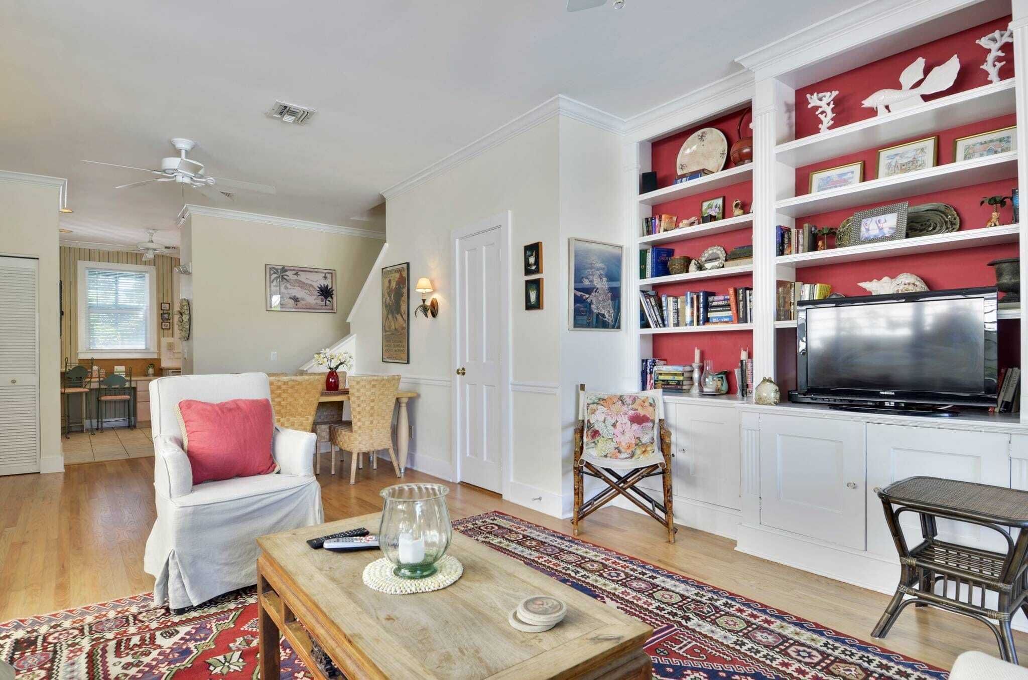 A living room with a white armchair, a coffee table, a television, and a bookshelf with various decorative items.
