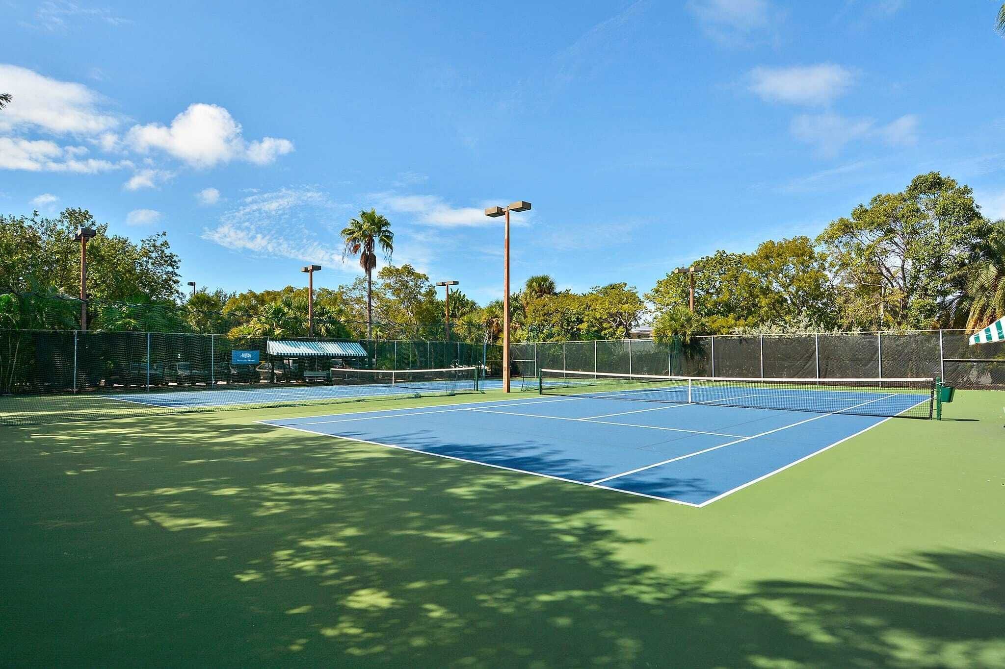Una cancha de tenis al aire libre con red, rodeada por una valla y árboles.