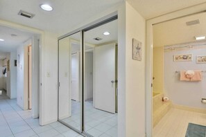 Habitación de hotel con puerta corredera de vidrio que da al baño, piso de baldosas y una pequeña alfombra.