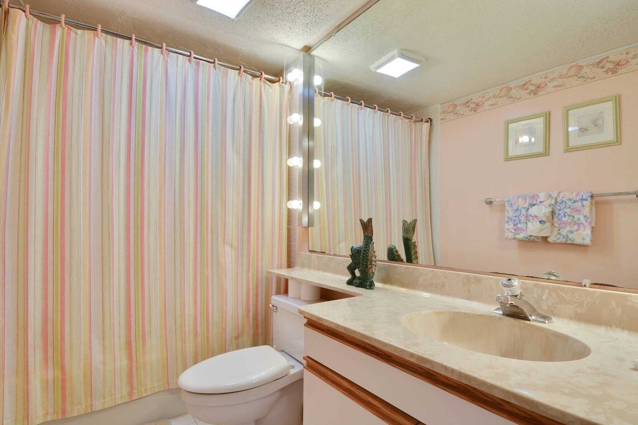A bathroom with a striped shower curtain, a sink with a mirror, and a toilet.