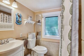 A bathroom with a sink, toilet, and window. There are shelves with towels and a decorative mirror.