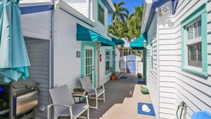 A narrow wooden pathway between two white buildings with teal accents, leading to a covered seating area with chairs and a table. - Windchime by Avantstay Walk to Duval Street Month Long Stays Only (Key West)