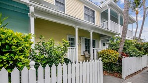A two-story house with a porch, white picket fence, and green foliage. - Always Your Paradise by Avantstay Shared Pool Near Zachary Beach! Month-long Stays Only (Key West)