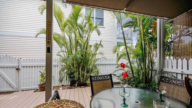 A covered patio with a round glass table, chairs, and potted plants. - Always Your Paradise by Avantstay Shared Pool Near Zachary Beach! Month-long Stays Only (Key West)