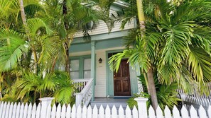 A house with a porch, a white picket fence, and lush green foliage.