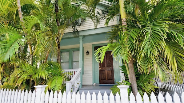 A house with a porch, a white picket fence, and lush green foliage.