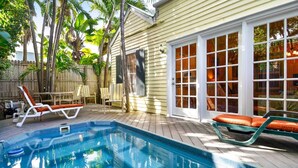 A swimming pool with two sun loungers, a wooden deck, and a house with a large window and a door. - Key Lime Pie by Avantstay Ideal Location w/ Splash Pool & Out Door Dining Month Long Stays Only (Key West)