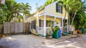 A single-story house with a porch, surrounded by a wooden fence and palm trees. - Key Lime Pie by Avantstay Ideal Location w/ Splash Pool & Out Door Dining Month Long Stays Only (Key West)