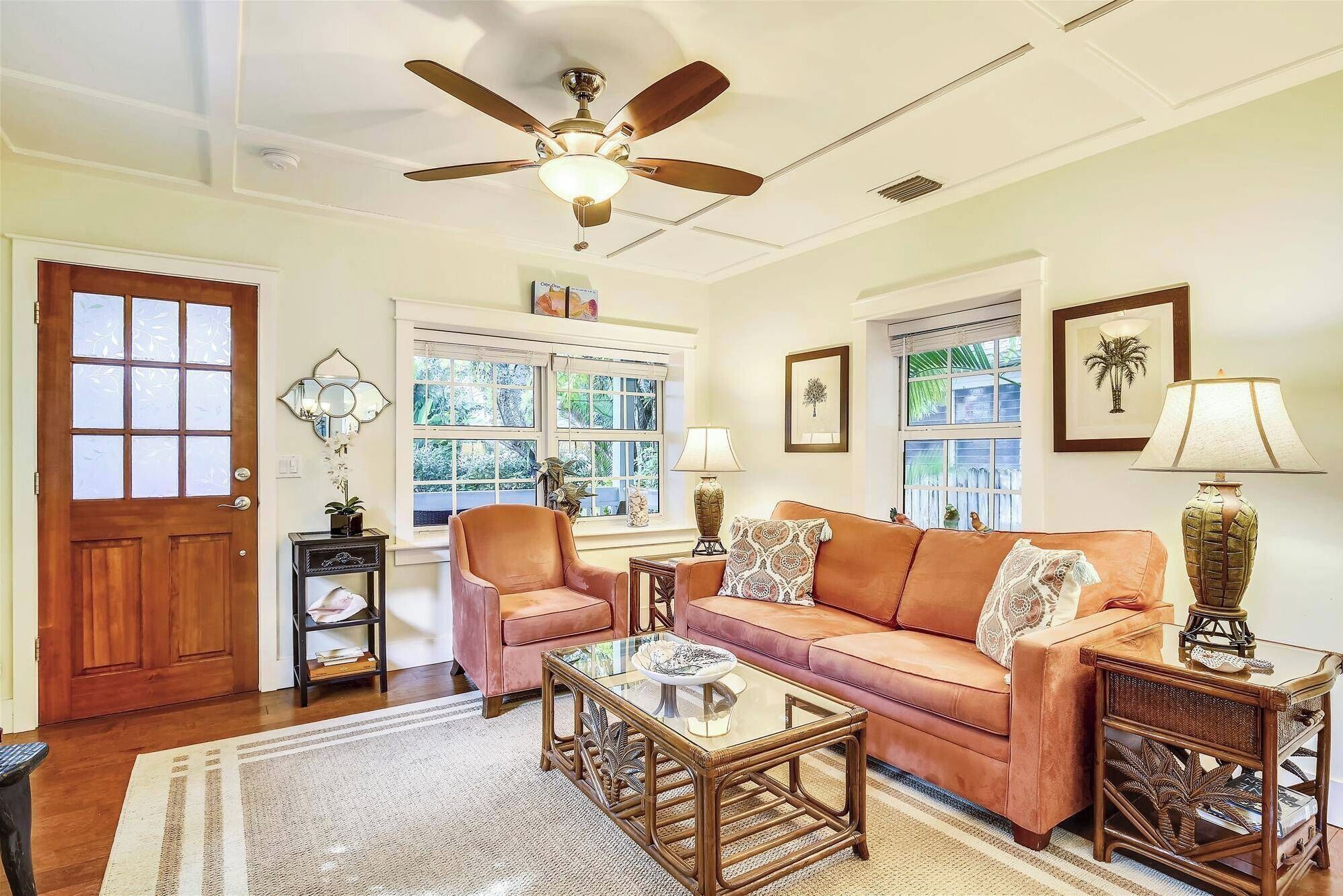A living room with a ceiling fan, a wooden door, a sofa, a glass coffee table, and two lamps.