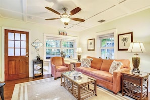 A living room with a ceiling fan, a wooden door, a sofa, a glass coffee table, and two lamps.