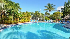 A swimming pool with blue tiles, surrounded by palm trees and lounge chairs. - Brisa Del Mar by Avantstay Communal Pool Gated Community Ocean Front (Key West)