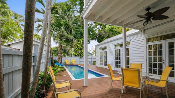 Un espace extérieur abrité avec une piscine, des chaises jaunes et un ventilateur de plafond.