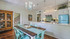 Une cuisine dotée d’un îlot central, de meubles blancs et d’un réfrigérateur bleu, ainsi que d’un lustre.