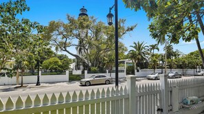 Une vue de rue avec une clôture blanche en bois, des voitures garées et un phare en arrière-plan.