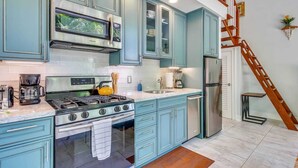 Uma cozinha com armários verde-água, eletrodomésticos de aço inoxidável e uma escada de madeira.