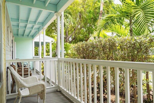 A porch with white railings, wicker chairs, and a view of lush greenery.