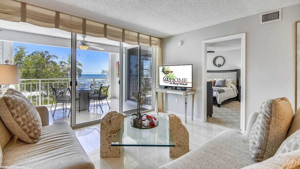 Una sala de estar moderna con una mesa de centro de vidrio, un sofá y un televisor que muestra 'a HOME en Key West'.
