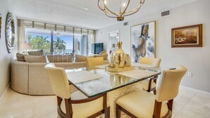 Un amplio salón con mesa de vidrio para comedor, asientos cómodos y un ventanal con vistas a palmeras.