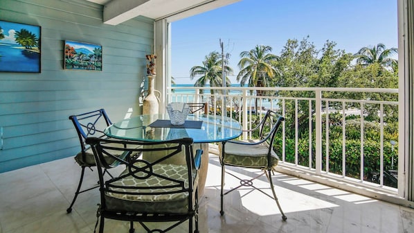 Ein Balkon mit Glastisch und Stühlen, Blick aufs Meer und tropische Pflanzen.