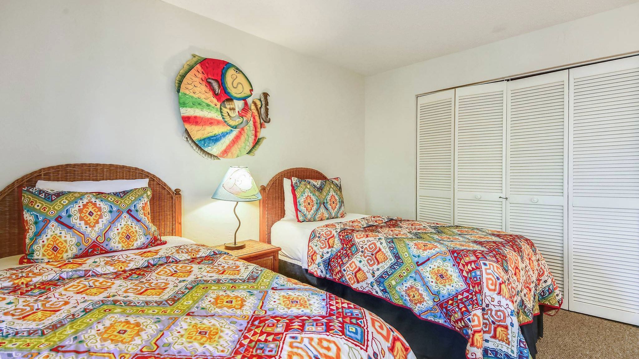 A room with two beds, a wall art piece, a lamp, and a closet.