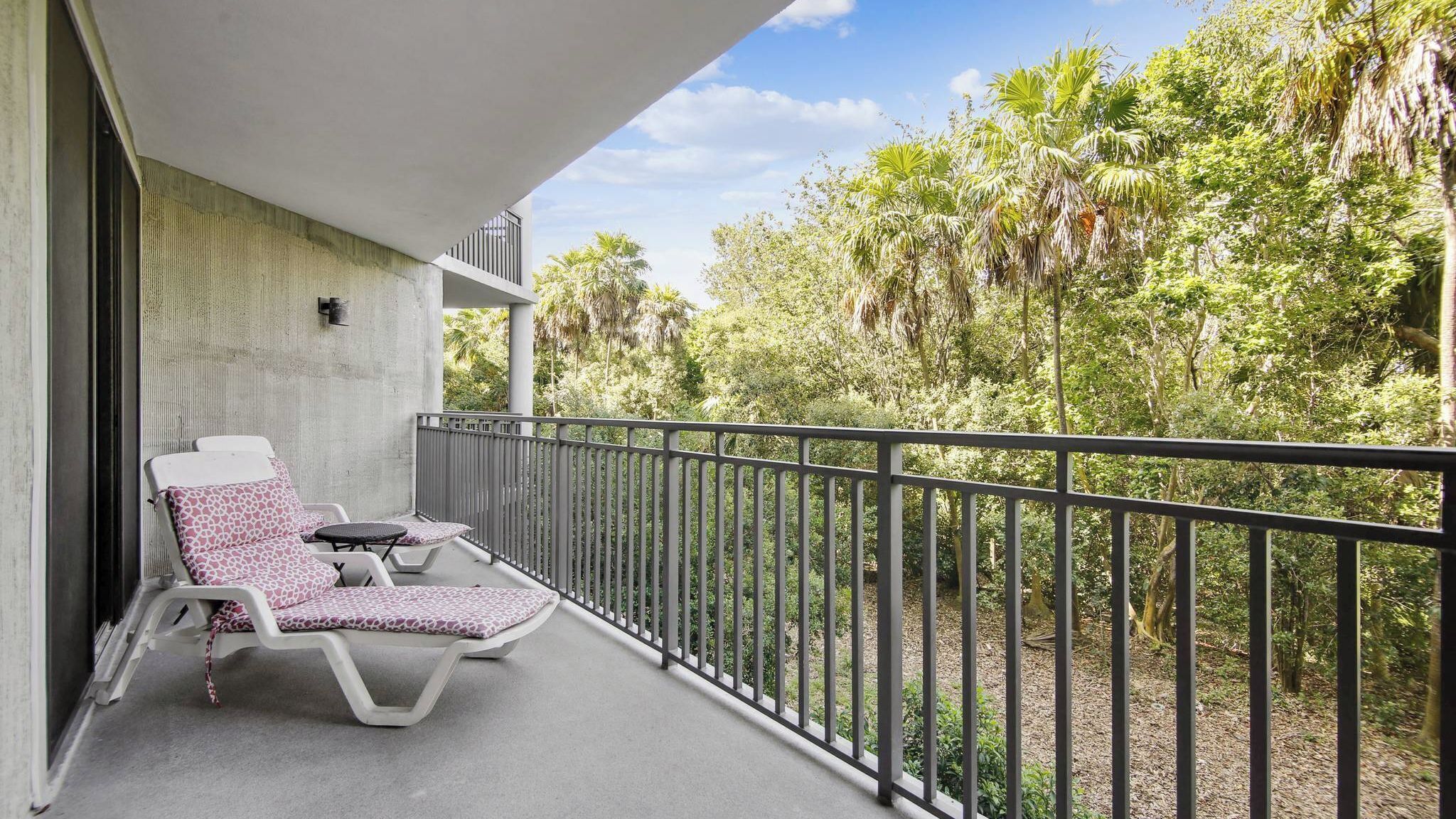 Un balcon avec deux chaises longues, un mur en béton et une vue sur un feuillage dense.