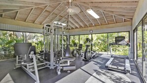 Une salle de sport équipée de divers appareils d’exercice, dotée de grandes fenêtres et d’un ventilateur de plafond.