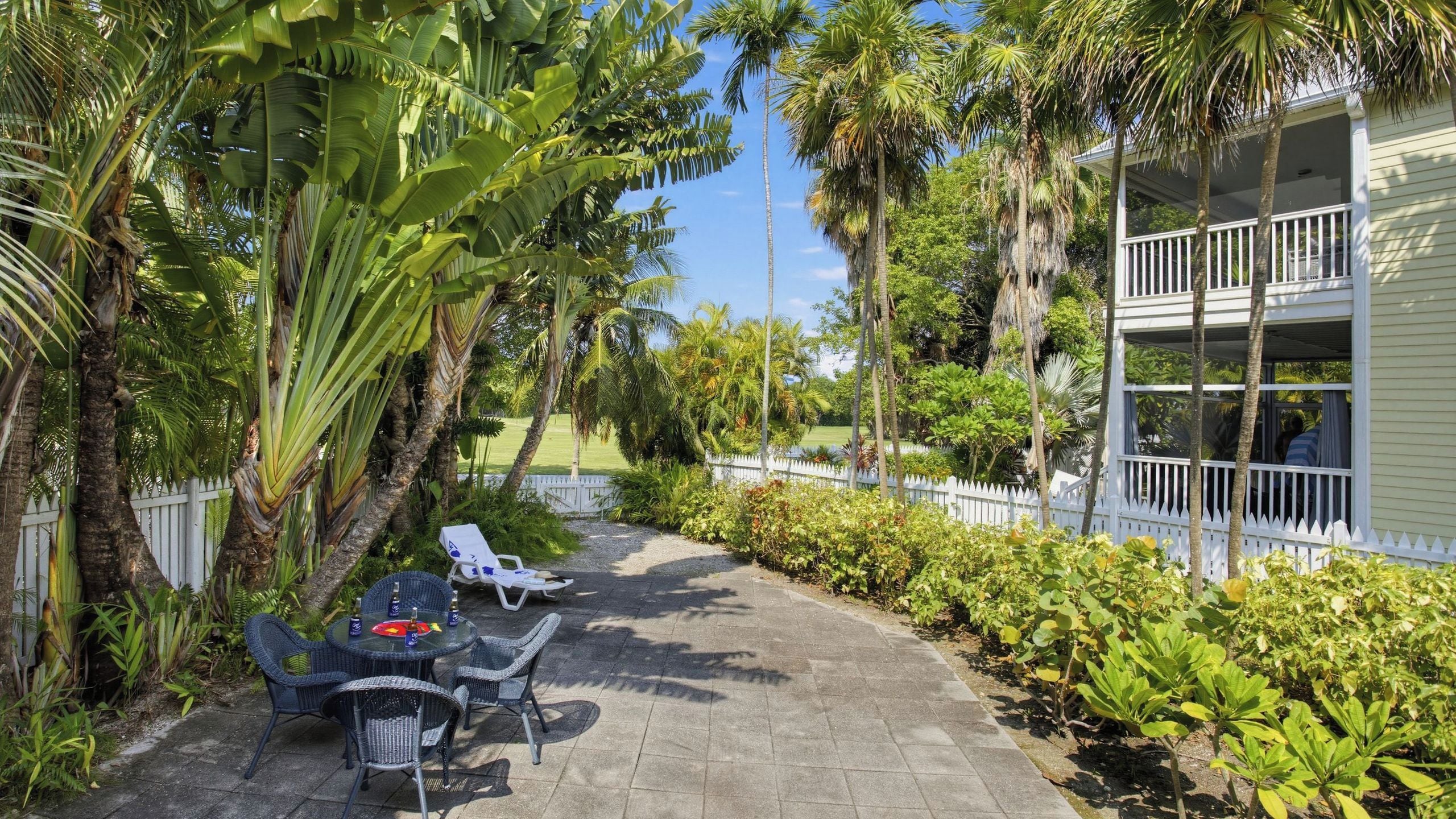 A patio with outdoor furniture, a white fence, and lush greenery.