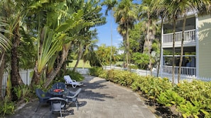 A patio with outdoor furniture, a white fence, and lush greenery.