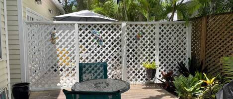 A covered patio with a table and chairs, surrounded by a white lattice fence, and various potted plants.