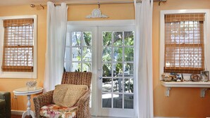 A room with a wicker chair, a small table, and a view through a glass door to an outdoor area. - Tranquility by Avantstay Close to Duval St w/ BBQ & Shared Pool (Key West)