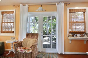 A room with a wicker chair, a small table, and a view through a glass door to an outdoor area.