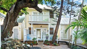 A two-story house with a porch, a stone pathway, and a large tree in the foreground. - Tranquility by Avantstay Close to Duval St w/ BBQ & Shared Pool (Key West)