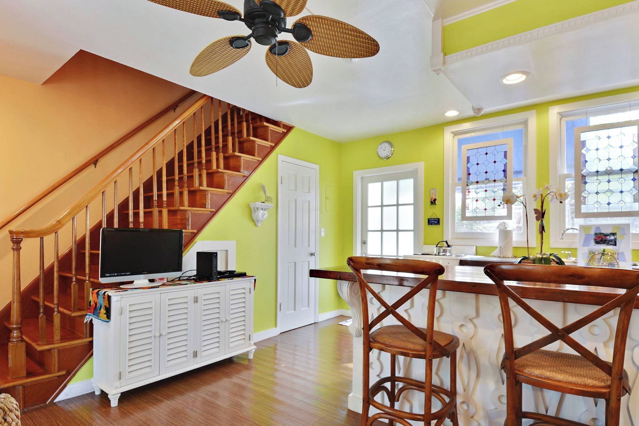 A kitchen with a wooden staircase, a ceiling fan, and a bar area with chairs.