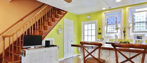A kitchen with a wooden staircase, a ceiling fan, and a bar area with chairs.