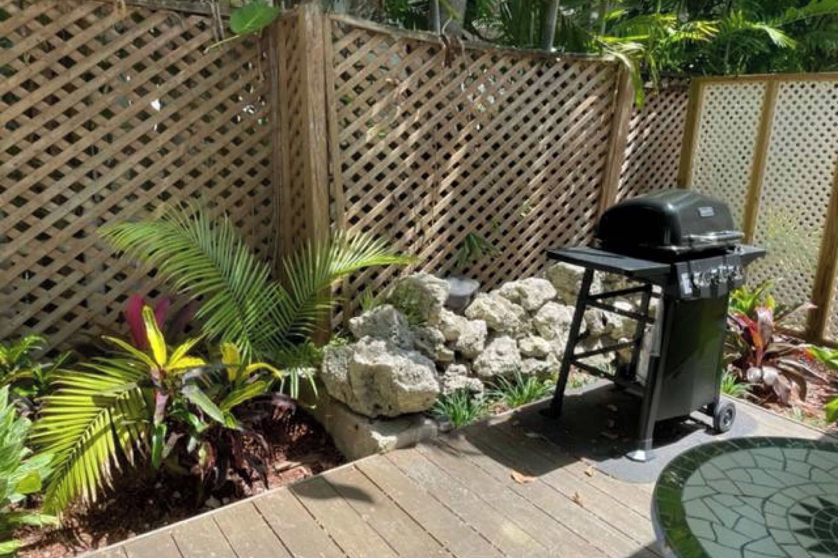 A patio area with a grill, a wooden deck, and a lattice fence.