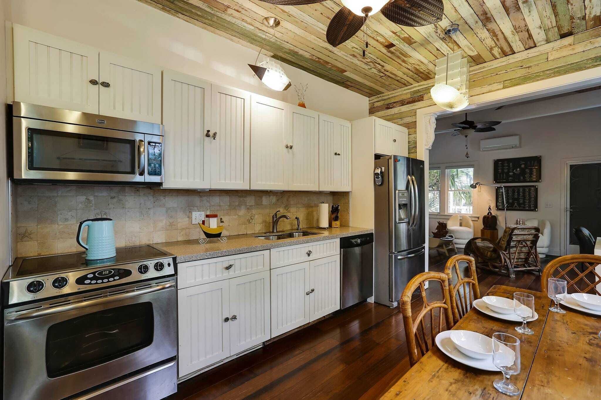 A modern kitchen with white cabinetry, stainless steel appliances, and a wooden dining table set for four.