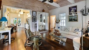 A spacious living room with wooden floors, a white sofa, and a dining area with a table and chairs. - Boat House by Avantstay Character Cottage Central Location w/ Shared Pool Month Long Stays (Key West)